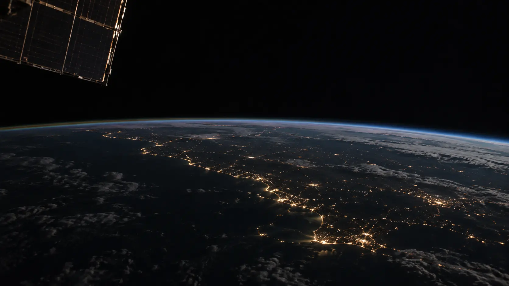 Earth at night seen from orbit, city lights along a coastline